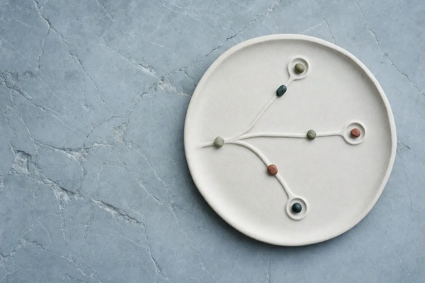 A porcelain tray with branching channels and colored stones, evoking a workflow plan